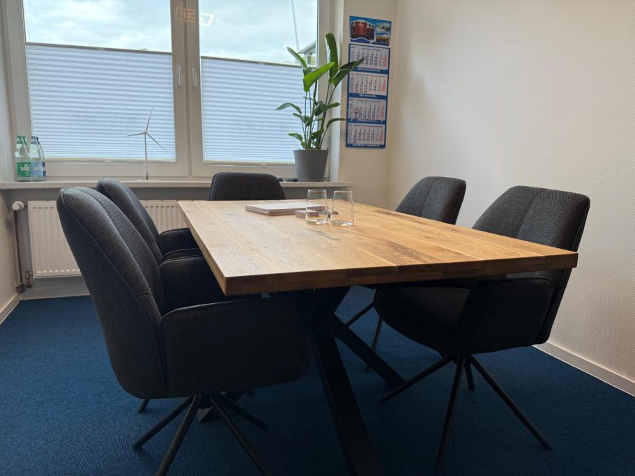 Besprechungsraum Besprechungstisch aus Holz mit fünf grauen Stühlen und Pflanze in der Ecke
